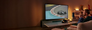 A father and son smiling while watching a high-speed auto race on TV, with WiZ Smart Lighting behind the screen and on nearby shelves.